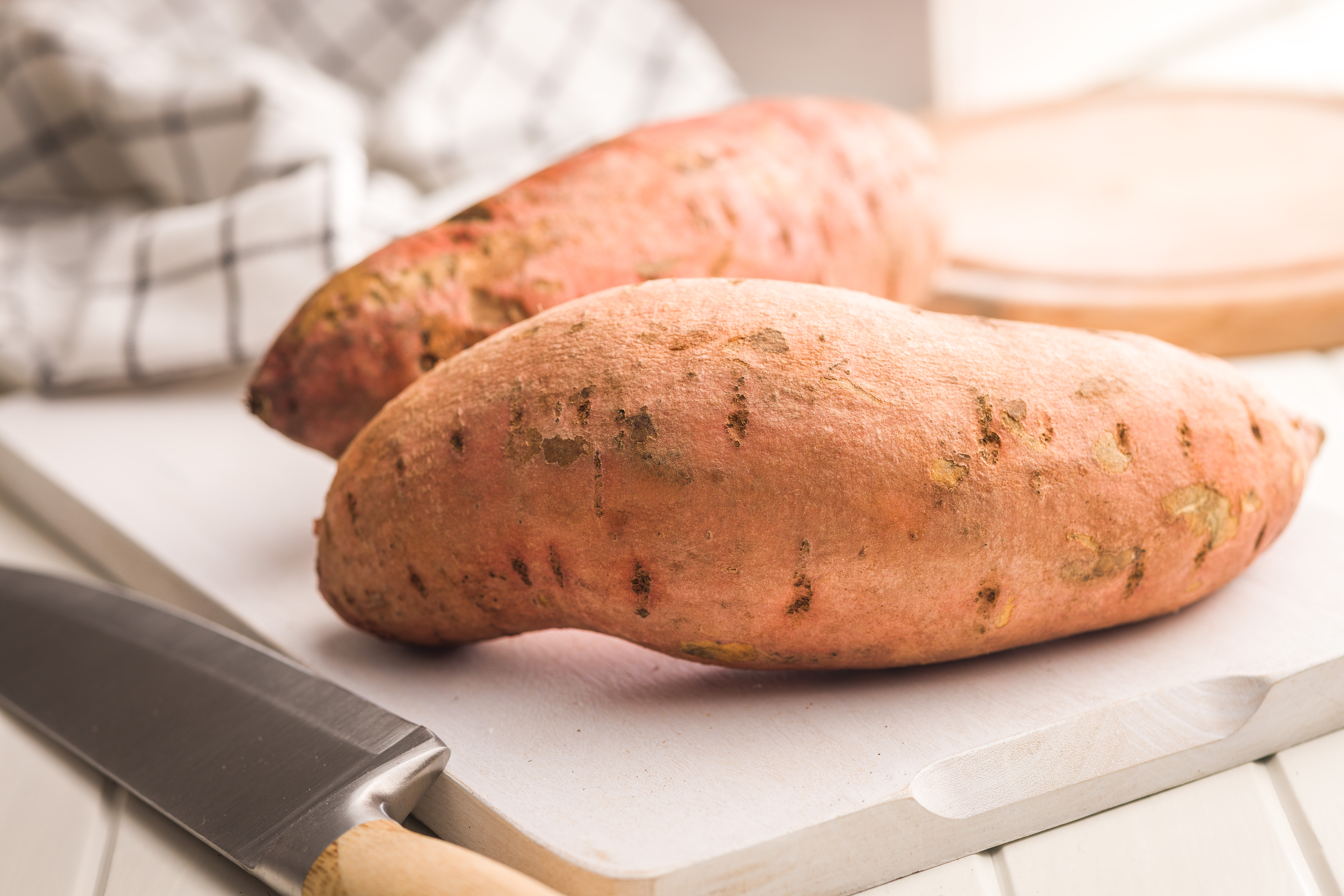 Raw sweet potatoes on cutting board on a white table.