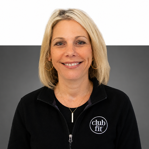 Women with short blonde hair smiles infront of half grey half white background, wearing club fit jacket.